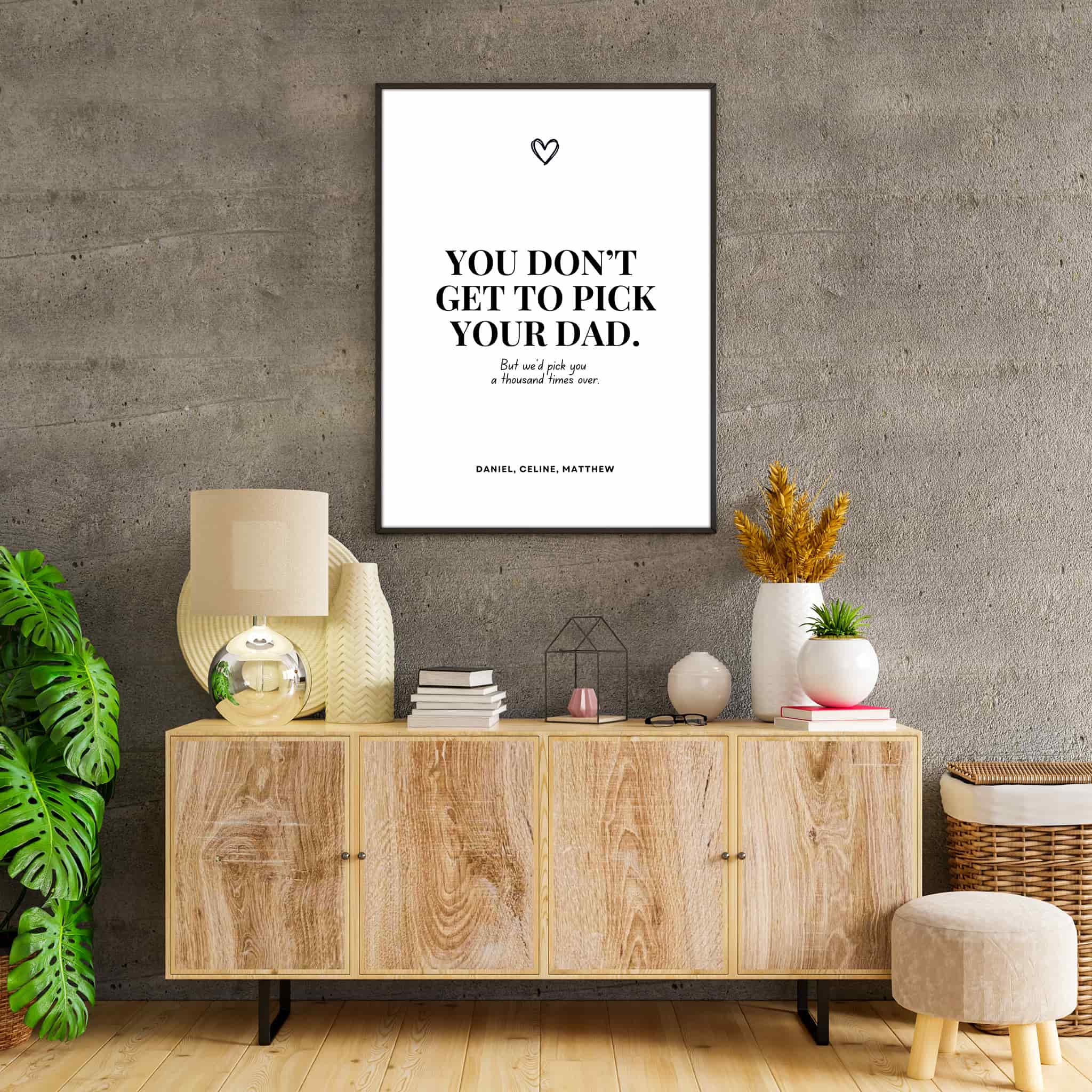 Black and white poster with the quote ‘You don’t get to pick your dad. But we’d pick you a thousand times over,’ personalized with children’s names and a small heart symbol above, hanging on the wall of a cozy living room.